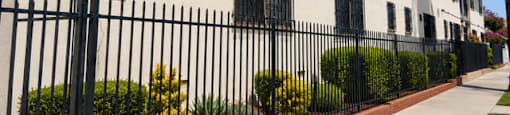A white building with black iron fencing and bushes in front.