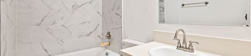 A white bathroom with a marble wall and a white tub.