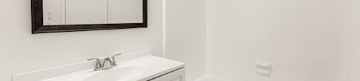 A white bathroom with a sink, mirror, and bathtub.
