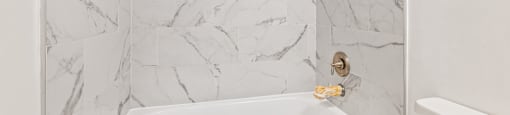 A white bathtub with a marble wall behind it.