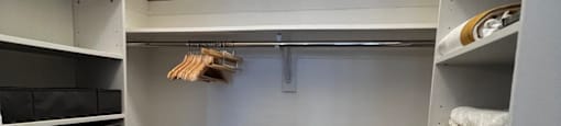 a walk in closet with white shelves and a wood floor