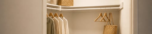 A small, well-lit closet with clothes hanging on a rail and a basket on the floor.