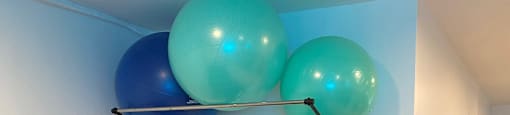A room with a blue exercise ball suspended from the ceiling and a green yoga mat on the floor.