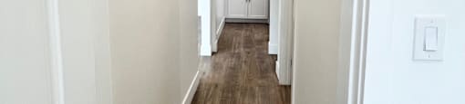 a long hallway with white walls and wood floors and a kitchen in the distance