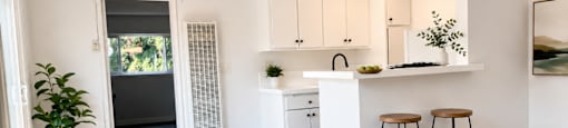 A kitchen with white cabinets and a white island with two stools.