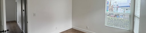 A room with wooden flooring and a window with blinds.