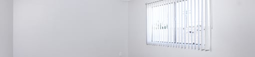 A room with a carpeted floor and a window with blinds.