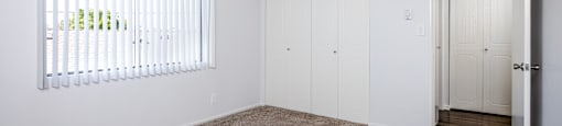 A room with a carpeted floor, a window with blinds, and a door.