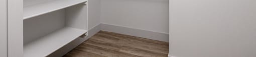 a walk in closet with white walls and shelves and a wood floor