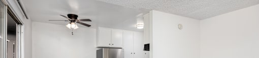 an empty living room with a kitchen and a ceiling fan