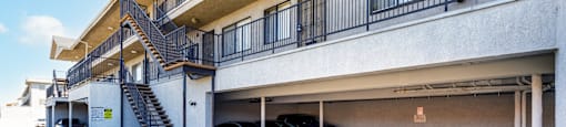 A car is parked in a garage under a building with a balcony.