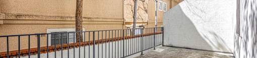 A tree is in front of a building with a white wall and a black fence.