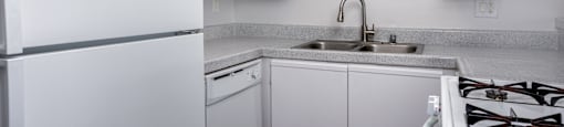 A white kitchen with a refrigerator, sink, and stove.