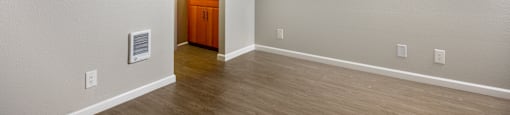 A room with a wooden floor and a white wall with a doorway leading to another room.