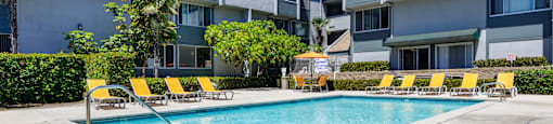a swimming pool with yellow chairs in front of an apartment building