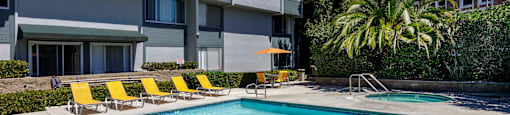 a swimming pool with yellow chairs in front of a building
