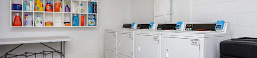 a laundry room with four washers and dryers and a table with a shelf