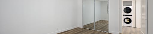 a living room with white walls and wood floors and a mirrored closet