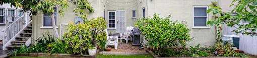 the backyard of a white apartment building with a lawn and plants