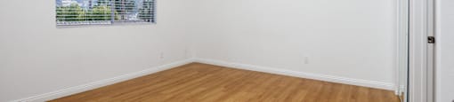 an empty living room with wood floors and a window