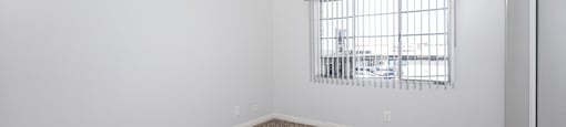 A room with a carpeted floor and a window with bars.