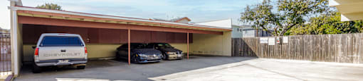 A carport with a white van and a black car parked inside.