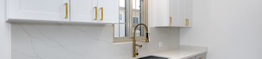 a kitchen with white cabinets and a sink and a gold faucet
