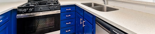 A kitchen with blue drawers and a stove top oven.