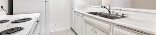A white kitchen with a stove, sink, and cabinets.