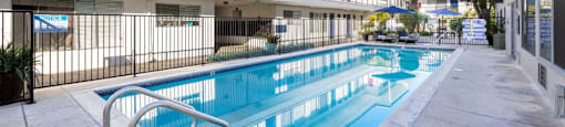 A long rectangular pool in front of a building with a balcony.