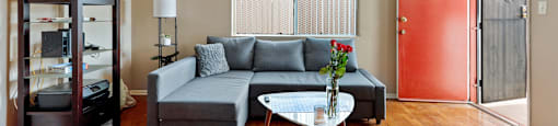 A living room with a grey couch, a white coffee table, a ceiling fan, and a red door.