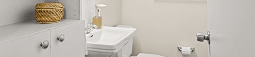 a white bathroom with a white toilet and sink and a white cabinet with a green plant on