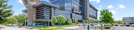 A modern building with a glass facade is surrounded by trees and a clear blue sky.