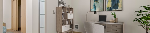 A room with a desk, chair, and a plant.