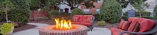 A fire pit in the middle of a patio surrounded by chairs and plants.