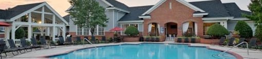 A large swimming pool in front of a house with a patio and lounge chairs.