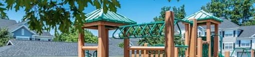 A playground with a green slide and wooden play structure.