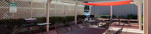 A patio with a table and chairs under a red shade sail.