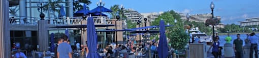 A group of people are sitting at tables under blue umbrellas on a patio.  at The 925 Apartments, Washington, DC