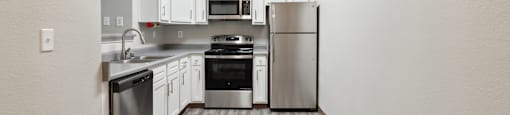 an empty kitchen with stainless steel appliances and white cabinets
