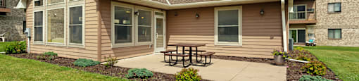 A house with a brown roof and tan siding has a picnic table in front of it.