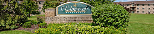 A sign that says "Elmcroft Apartments" in front of a building.