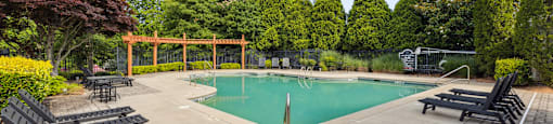 a swimming pool with black chairs and a fence and trees