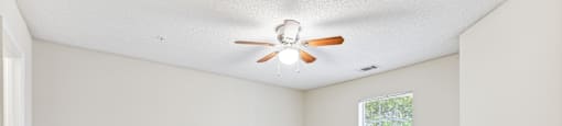 an empty living room with a ceiling fan and a window
