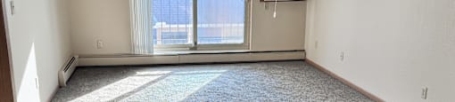 A room with a carpeted floor, a window with blinds, and a wall-mounted air conditioning unit.