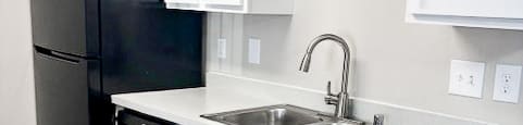 A black refrigerator is in a kitchen with white cabinets.