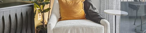 a chair with a yellow pillow in a room with a window and a plant
