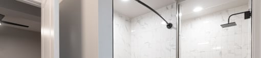 A white marble patterned shower area with a white bathtub and a glass door.