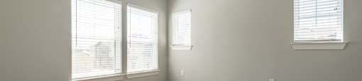 an empty living room with three windows and a ceiling fan