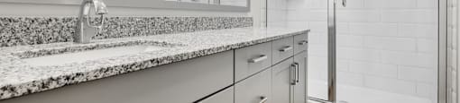 a bathroom with white cabinets and granite counter tops and a shower
